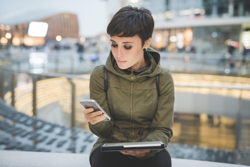 Woman in green coat using mobile and tablet